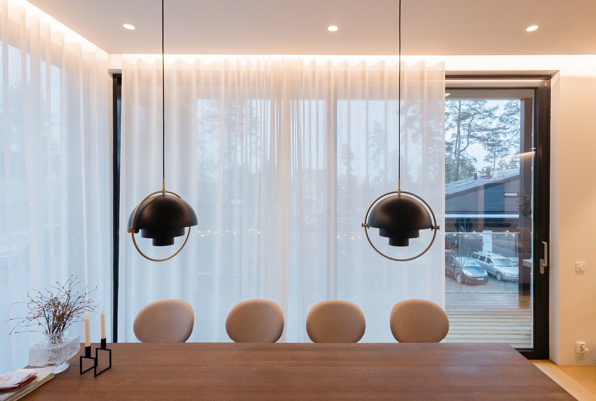 La zona pranzo è illuminata da strisce LED dietro tende a luce naturale, faretti a incasso sul soffitto e due luci a sospensione sul tavolo.